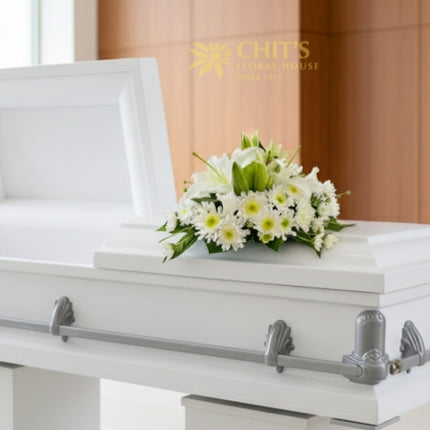 Elegant funeral casket flower arrangement featuring white lilies, chrysanthemums, and foliage symbolizing purity and peace. Handcrafted by Chits Floral House.