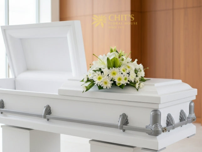 Elegant funeral casket flower arrangement featuring white lilies, chrysanthemums, and foliage symbolizing purity and peace. Handcrafted by Chits Floral House.